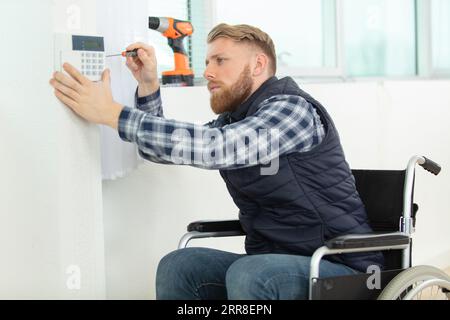 young electrician in wheelchair installing security alarm on wall Stock Photo