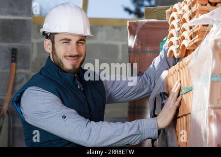 young bricklayer near red brick stack in building under construction Stock Photo