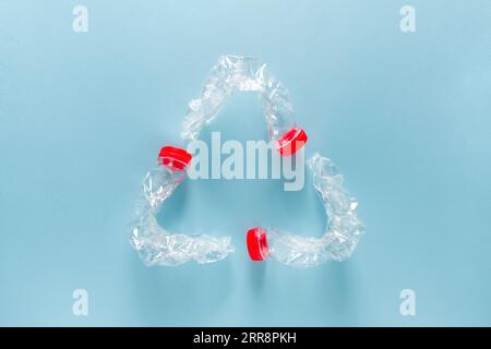 Three blue plastic water bottles bent together to form a recycling symbol on a blue background Stock Photo