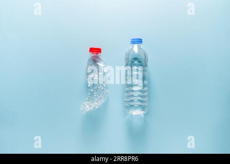 Plastic water bottle filled with empty and crushed plastic water bottle standing side by side on blue background Stock Photo
