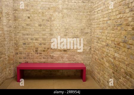 Simple Pink wooden bench in an empty brick room. Stock Photo