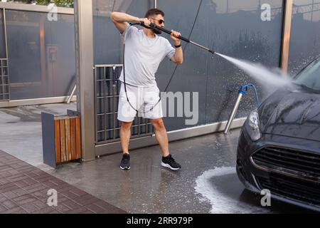 A man washes the front of a car with a water cannon. A car at a self service car wash. Stock Photo