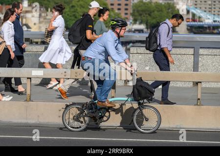 A man riding a Brompton folding bicycle across London Bridge, London, UK.  17 Jul 2023 Stock Photo