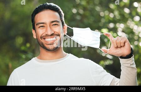 Portrait, mask and remove with a man breathing fresh air in nature, feeling happy at the end of restrictions. Covid, freedom and smile for post Stock Photo