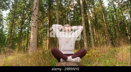 Sporty woman taking a break, sitting in a forest after exercise catching her breath. Stock Photo