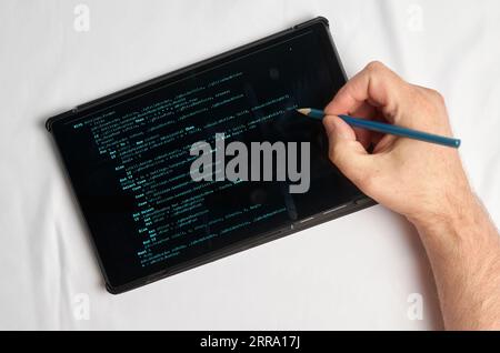 Programming and coding concept. A hand with a pencil writes a program listing on the screen Stock Photo