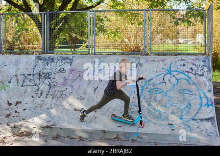 Child on kick scooter in park. Kids learn to skate roller board. Little boy skating on sunny summer day. Outdoor activity for children on safe residen Stock Photo