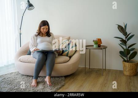 In a heartwarming connection, an Asian expectant mother reads tales to her unborn child, weaving dreams and love through each gentle word. Stock Photo