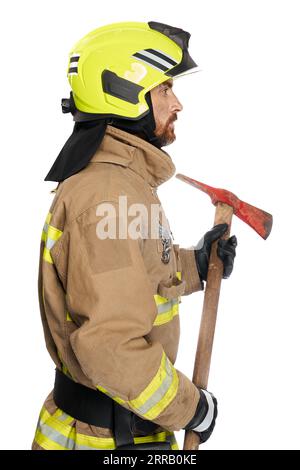 Focused male fireman using wooden axe tool for work. Side view of middle-aged man in fire uniform with hatchet looking away, isolated on white studio background. Job, equipment, tool concept. Stock Photo