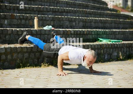 Muscular, senior man in sportswear training outdoors, doing push ups exercises on stairs Stock Photo