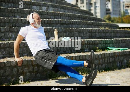 Muscular, senior man in sportswear training outdoors, doing reverse push ups exercises on stairs Stock Photo