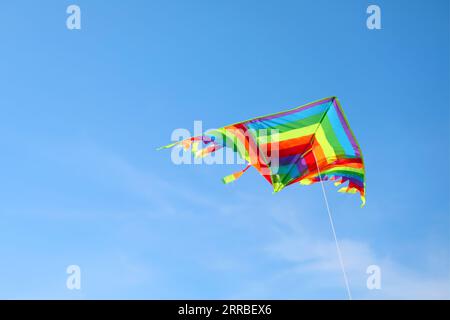 multicolored kite with long colorful tail flying free in the blue sky Stock Photo