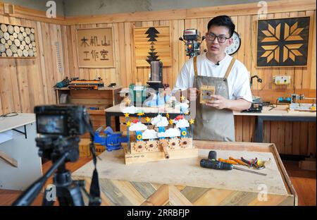 210919 -- SHIJIAZHUANG, Sept. 19, 2021 -- Li Zhanlong records a lesson to be posted on social media at his studio in Luquan District of Shijiazhuang, north China s Hebei Province, Sept. 15, 2021. Li Zhanlong is a wooden mechanical installation designer in Shijiazhuang. After graduation, Li once worked as a salesman and ran an online shop. In 2018, Li Zhanlong left his job and went to Tianjin to learn carpentry skills. The wooden mechanical installation consists of a wooden figure and a mechanism device that can make the installation move. By shaking the handle or pressing the button, the insta Stock Photo