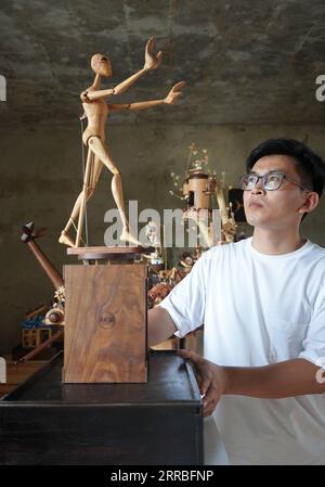 210919 -- SHIJIAZHUANG, Sept. 19, 2021 -- Li Zhanlong shows a wooden mechanical installation at his studio in Luquan District of Shijiazhuang, north China s Hebei Province, Sept. 14, 2021. Li Zhanlong is a wooden mechanical installation designer in Shijiazhuang. After graduation, Li once worked as a salesman and ran an online shop. In 2018, Li Zhanlong left his job and went to Tianjin to learn carpentry skills. The wooden mechanical installation consists of a wooden figure and a mechanism device that can make the installation move. By shaking the handle or pressing the button, the installation Stock Photo