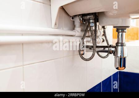 new white polypropylene pipes connect with faucet under sink in bathroom on wall covered with ceramic tiles Stock Photo