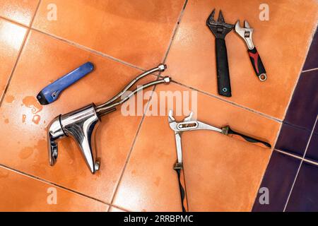 top view of wrenches and plumbing tools and removed old faucet on ceramic tiles on bathroom floor Stock Photo