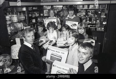 1981, inside a home appliances or electrical shop, a male shopkeeper  with excited young school children with their prizes of the latest portable transistor radios and cassette recorders, England. UK. The young wnners are holding  the Pye Radio Model 1420, while the cassette recorder is a Pye Model 9110. The Pye brand dates back to 1896 when William Pye started making scientific instruments in Cambridge under the name W. G Pye Ltd and then 1922 wireless components. In 1928 Pye sold the business, now called Pye Radio Ltd to C.O Stanley. Stock Photo