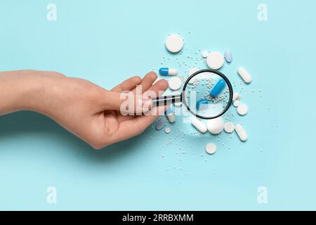 Female hand with magnifier and pills on blue background Stock Photo