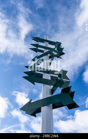 white sign post with many dark green blank arrows and a blue sky with white clouds Stock Photo