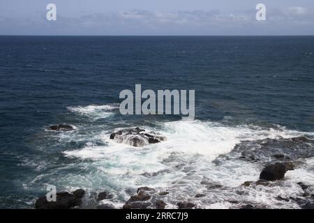 Landscape in front of the blue sea that meets the sky and in which the waves crash against rocks near the coast of the island Stock Photo