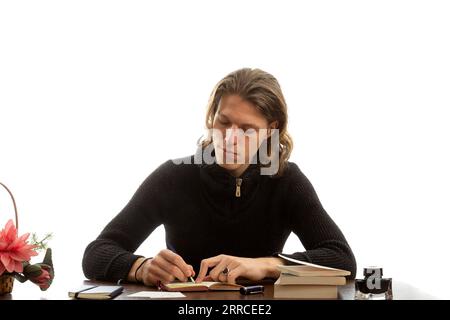 Handsome young writer sitting at the table and writing  Stock Photo