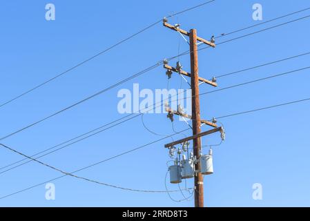 Wooden post supporting high voltage cables and transformers against blue sky Stock Photo