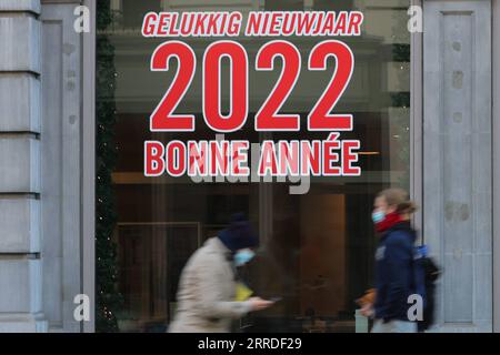 211221 -- BRUSSELS, Dec. 21, 2021 -- People walk past a window with words Happy New Year 2022 in Brussels, Belgium, on Dec. 21, 2021. Belgium is in the midst of a new wave of COVID-19 pandemic due to the Omicron variant, which represented 20 percent of all positive test results across the country reported Monday morning, according to microbiologist Emmanuel Andre.  BELGIUM-BRUSSELS-COVID-19-OMICRON VARIANT ZhengxHuansong PUBLICATIONxNOTxINxCHN Stock Photo