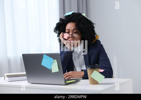 Deadline concept. Tired woman working with laptop in office. Many sticky notes everywhere as reminders Stock Photo