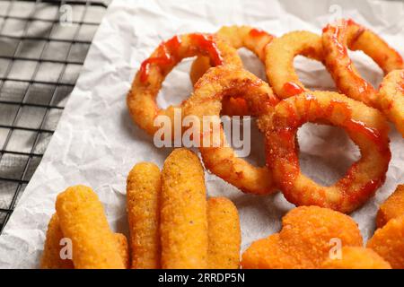 Tasty chicken nuggets, fried onion rings, cheese sticks and ketchup on parchment paper, closeup Stock Photo