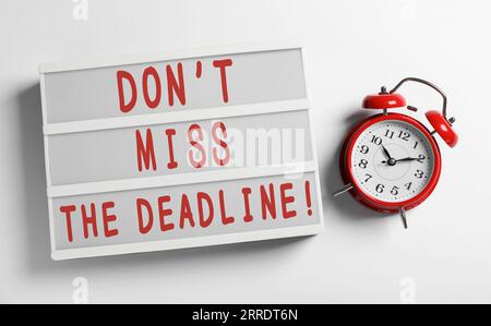 Light box with reminder Don't Miss The Deadline and alarm clock on white background, flat lay Stock Photo