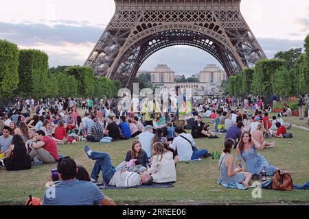 Souvenir sellers working on Champs de Mars sell keepsakes, beer and wine to tourists picnicking in the evening awaiting the Eiffel Tower light show Stock Photo