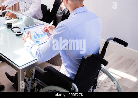 Disabled Male Manager Sitting With His Colleagues At Workplace Stock Photo
