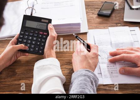 Close-up Of Couple Calculating Bills Using Calculator On Wooden Table Stock Photo