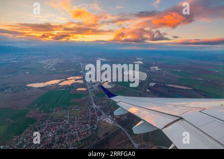 Airplane flight in sunset sky over city and wing of plane. View from the window of the Aircraft. Traveling in air. Stock Photo