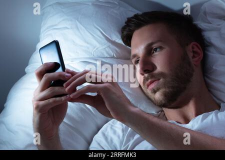 Young Man Using Cellphone In Bed At Night Stock Photo