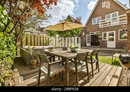 a patio with chairs and an umbrella over the table in front of a large brick house on a sunny day Stock Photo