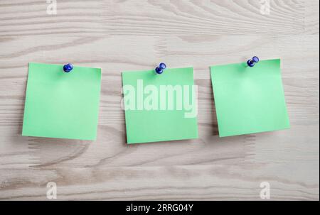 Three green paper notes mockup pinned to wooden bulletin board. sticky notes on bulletin board. Three green sticker with push pins on wooden backgroun Stock Photo