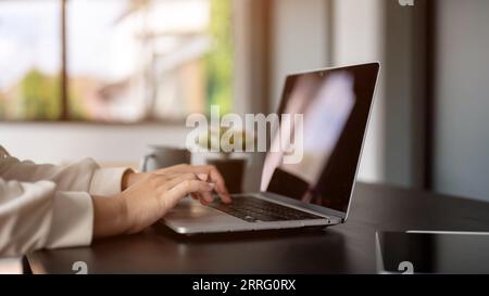 Close-up rear view image of a businesswoman working on her laptop computer at her desk in the office, typing on laptop keyboard, searching or browsing Stock Photo