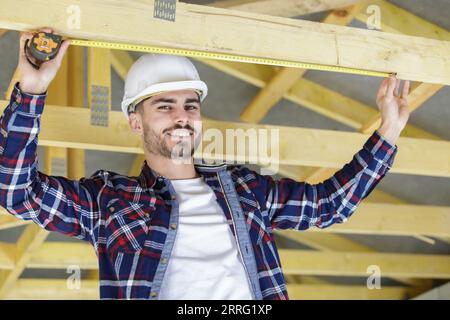happy worker in his 30s measures wood-beam with measuring tape Stock Photo