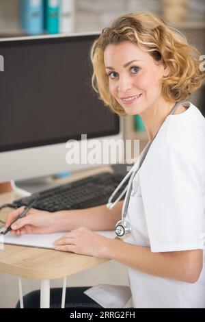 female doctor sat at computer desk writing notes Stock Photo