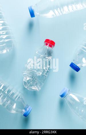 Crushed plastic water bottles with blue caps standing around crushed plastic water bottle with red cap on blue background Stock Photo
