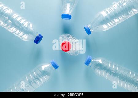Crushed plastic water bottles with blue caps standing around crushed plastic water bottle with red cap on blue background Stock Photo