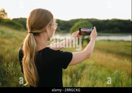 Back view of woman taking a video on smart phone of nature landscape Stock Photo