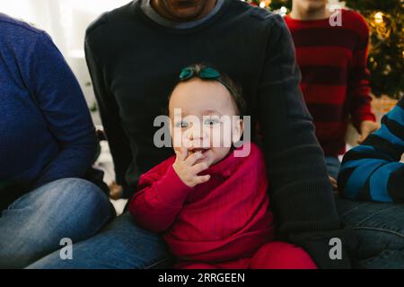Smiling baby girl on dads lap at christmas in multiracial family Stock Photo