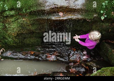 Child feeling waterfall coming down mossy cliff Stock Photo