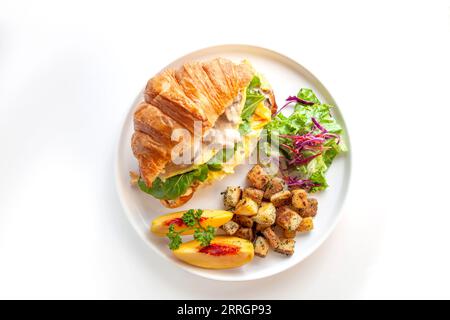 Brioche croissant scrambled egg Benedict with mushrooms and cream with sautéed potatoes and peach fruit. Stock Photo