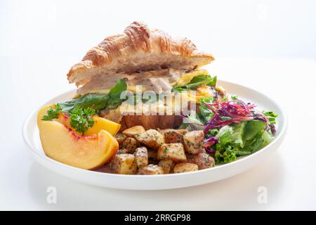 Brioche croissant scrambled egg Benedict with mushrooms and cream with sautéed potatoes and peach fruit. Stock Photo