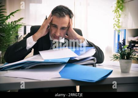 Detail of a businessman overworked over a pile of folders and reports overwhelmed in an office Stock Photo