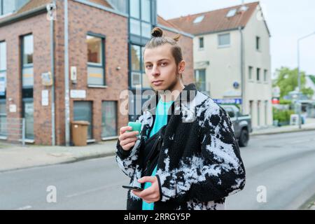 Young hipster male using smartphone, smoking disposable electronic cigarette Stock Photo