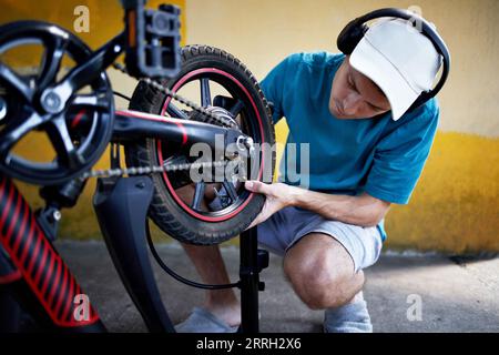 A young bicycle mechanic is repairing a bicycle in the yard of his house.  Stock Photo